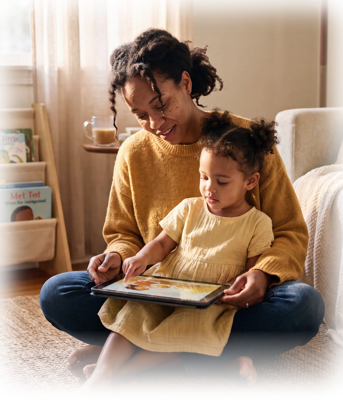 Mãe e filha lendo juntas um livro da coleção Com Jesus no tablet